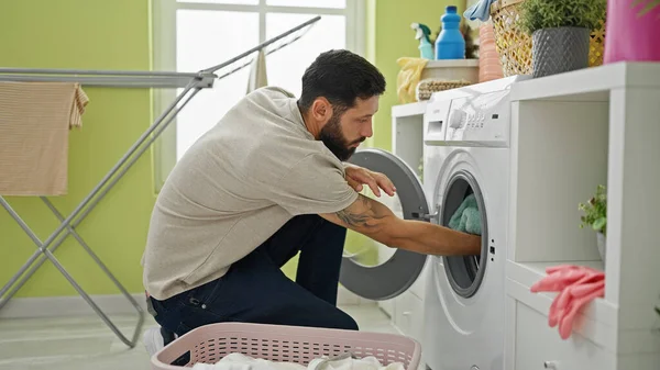 Young hispanic man washing clothes at laundry room