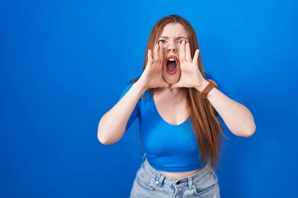 Roodharige Vrouw Staande Blauwe Achtergrond Schreeuwen Boos Hardop Met Handen — Stockfoto