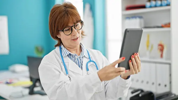 Middle age woman doctor doing video call with touchpad at clinic