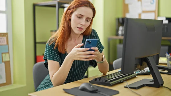 Młoda Ruda Kobieta Biznes Pracownik Pomocą Smartfona Poważną Twarzą Biurze — Zdjęcie stockowe