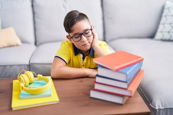 Adorable hispanic boy student sitting on floor with boring expression at home