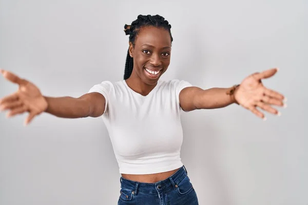 Beautiful black woman standing over isolated background looking at the camera smiling with open arms for hug. cheerful expression embracing happiness.