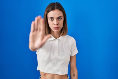 Hispanic woman standing over blue background doing stop sing with palm of the hand. warning expression with negative and serious gesture on the face. 