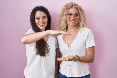 Anne ve kızı pembe arkaplanda el kol hareketleri yaparak büyük ve büyük boy işareti ve ölçü sembolü gösteriyorlar. Kameraya bakıp gülümsüyor. ölçüm kavramı. 