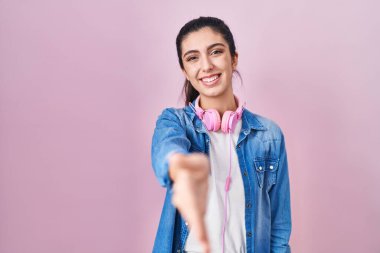 Pembe arka planda duran genç ve güzel bir kadın gülümseyerek selamlama ve hoş geldin demek için tokalaşıyor. başarılı iş. 