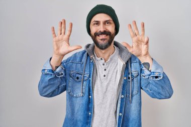 Dövmeli, yün şapkalı, dokuz numaralı parmaklarını gösterip gülümseyen, kendinden emin ve mutlu İspanyol bir adam.. 