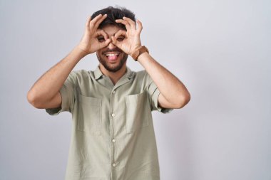 Beyaz arka planda duran sakallı bir Arap dürbün gibi jest yapıyor, gözleri parmaklarından bakıyor. çılgın ifade. 