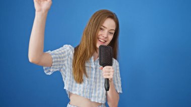 Genç sarışın kadın, mikrofon olarak fırçayı kullanarak şarkı söylüyor.