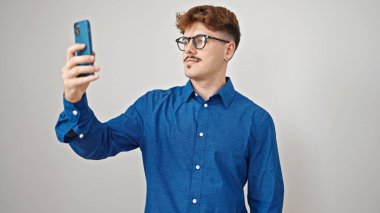 Genç İspanyol adam, izole edilmiş beyaz arka planda akıllı telefonun yanında selfie çekiyor.