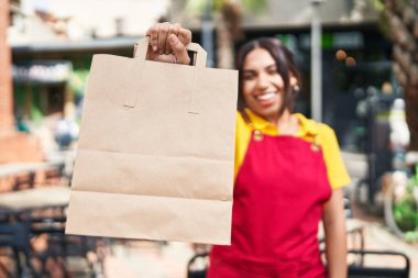 Young beautiful arab woman waitress smiling confident holding take away food at coffee shop terrace