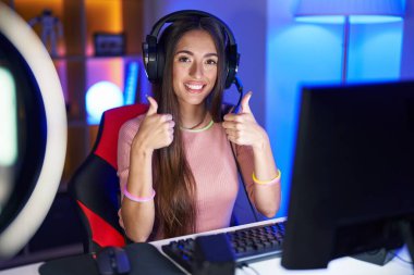 Genç İspanyol kadın video oyunları oynuyor. Elleriyle olumlu jest yapıyor. Gülümsüyor ve mutlu. Neşeli ifade ve kazanan jest. 