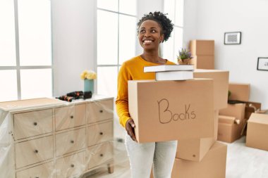 African american woman smiling confident holding books package at new home