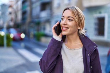 Gülümseyen genç bir kadın caddedeki akıllı telefondan konuşuyor.