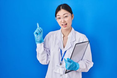 Çinli genç bir kadın bilim adamının laboratuarında çalışıyor. Yüzünde kocaman bir gülümseme var. Parmağıyla kameraya bakıyor.. 