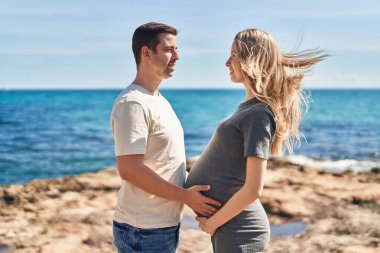 Erkek ve kadın bir arada, deniz kenarında göbeğe dokunuyorlar.