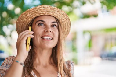 Young woman tourist wearing summer hat talking on smartphone at street
