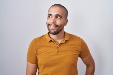 Hispanic man with beard standing over white background smiling looking to the side and staring away thinking. 