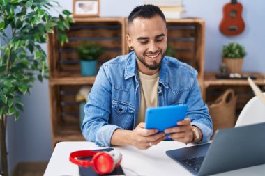 Young hispanic man using touchpad and laptop sitting on table at home