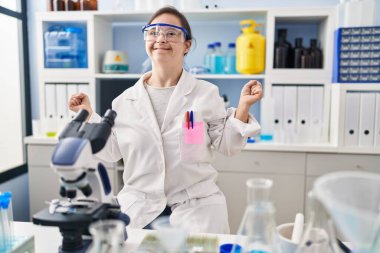 Down sendromlu İspanyol kız bilim adamlarının laboratuarında çalışıyor. Kolları havada ve gözleri kapalı bir şekilde başarıyı kutluyor ve şaşırıyor. Kazanan konsept. 