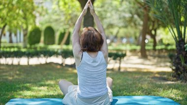 Orta yaşlı kadın parkta oturmuş yoga eğitimi alıyor.