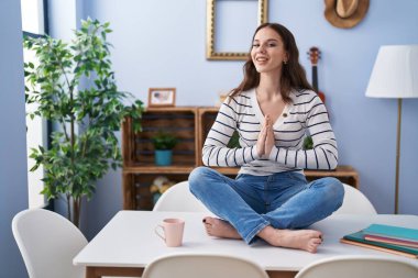 Young woman doing yoga exercise sitting on table at home