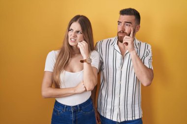 Sarı arka planda duran genç çift bir soru hakkında endişeleniyor, endişeli ve gergin. 