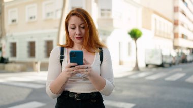 Caddede akıllı telefon kullanan genç kızıl saçlı kadın.