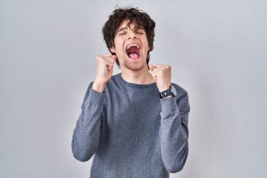 İzole edilmiş arka planda duran genç adam başarı için heyecanlı kolları havada ve gözleri kapalı zaferi kutlarken gülümsüyor. Kazanan konsept. 