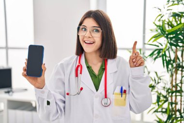 Zeki telefon ekranı gösteren genç İspanyol doktor bir fikir ya da soruyla şaşkın bir şekilde mutlu yüzle işaret ediyor. 