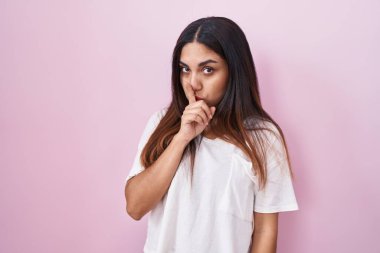 Pembe arka planda duran genç Arap kadın parmakları dudaklarında sessiz olmak istiyor. sessizlik ve gizli konsept. 