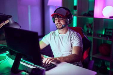 Young hispanic man streamer using computer and headphones at gamin room