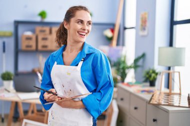 Young woman artist holding paintbrush and palette at art studio