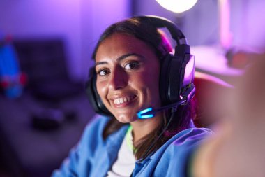 Young beautiful hispanic woman streamer smiling confident make selfie by camera at gaming room