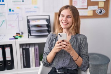 Ofiste çalışan sarışın iş kadını akıllı telefon kullanıyor.