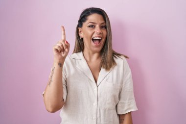 Pembe arka planda duran sarışın kadın başarılı bir fikir işaret ediyor. Heyecanlı ve mutlu. Bir numara.. 