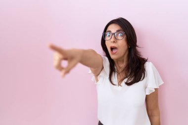 Orta yaşlı, beyaz tişörtlü ve gözlüklü bir İspanyol kadın parmağıyla işaret ediyor. İleride şaşırmış, ağzı açık, ön tarafta bir şey var. 