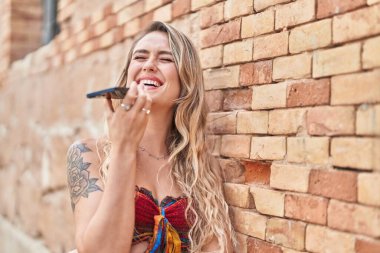 Genç sarışın kadın gülümsüyor. Kendine güveni tam. Akıllı telefondan konuşuyor.