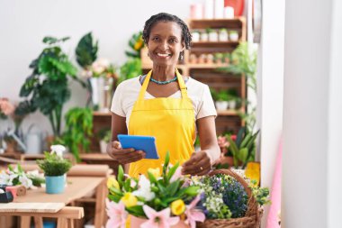 Middle age african american woman florist smiling confident using touchpad at flower shop