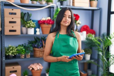 Çiçekçi dükkanında çalışan esmer kadın elinde tablet, yüzünde ciddi bir ifadeyle rahatlamış. Basit ve doğal bir şekilde kameraya bakıyorsun.. 