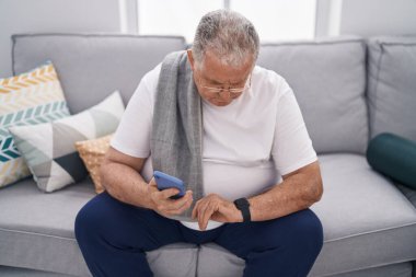 Orta yaşlı, kır saçlı, akıllı telefon kullanan, eve bakan bir adam.