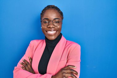 Beautiful black woman standing over blue background happy face smiling with crossed arms looking at the camera. positive person. 