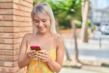 Sokakta akıllı telefon kullanan, kendine güvenen genç sarışın kadın.