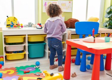 Adorable hispanic girl standing on back view at kindergarten