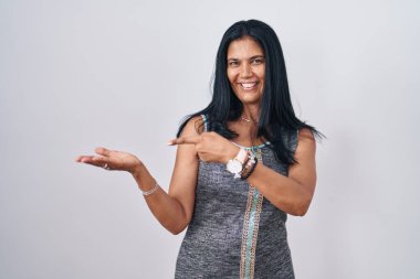 Beyaz arka planda duran olgun İspanyol kadın kameraya hayret ediyor ve gülümsüyor.. 