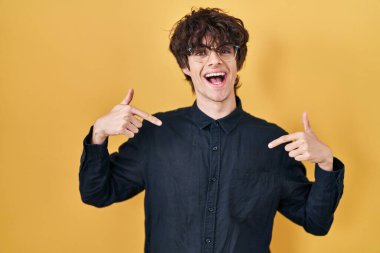 Sarı arka planda gözlük takan genç adam kendine güvenen, yüzünde gülümseme olan, kendini gururlu ve mutlu gösteren biri.. 