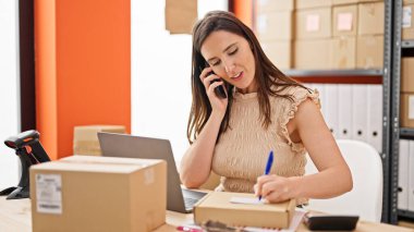 Genç ve güzel İspanyol kadın ecommerce iş işçisi. Ofisteki pakette akıllı telefon yazısıyla konuşuyor.