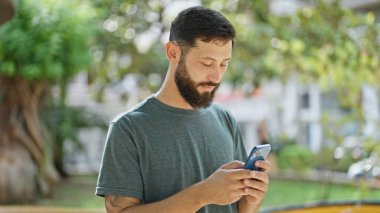 Genç İspanyol bir adam parkta akıllı telefon kullanıyor.