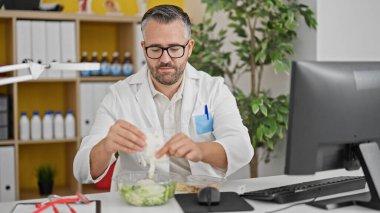 Klinikte çalışırken salata yiyen gri saçlı adam.