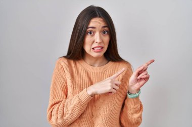 Beyaz arka plan üzerinde duran genç esmer kadın endişeli ve gergin iki elini de göstererek, endişeli ve şaşırmış yüz ifadesi 