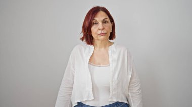 Soyutlanmış beyaz arka planda ciddi bir ifadeyle duran orta yaşlı kadın.